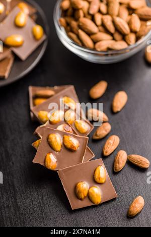 Broken chocolate bar with almonds on a black table. Stock Photo