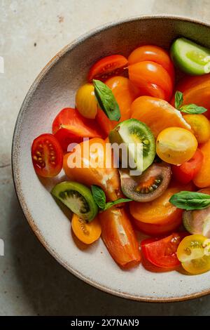 Close up of a bowl of coloured, fresh tomatoes with basil leaves Stock Photo