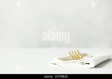 Golden Cutlery set and white napkin on light grey table with space for text. Festive table setting Stock Photo