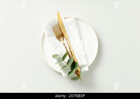 Gold Cutlery with eucalyptus branches on white plate with napkin over light grey Background. Minimalistic design. Copy Space Stock Photo