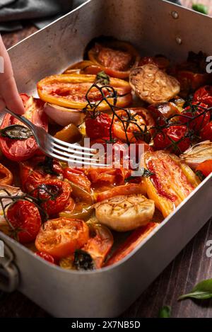 Fork pressing on baked fresh tomatoes, garlic, shallot, basil Stock Photo