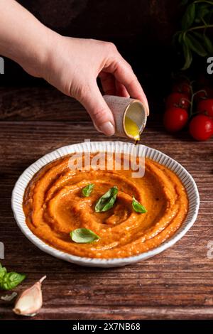 Hand pouring olive oil on fresh tomato sauce Stock Photo