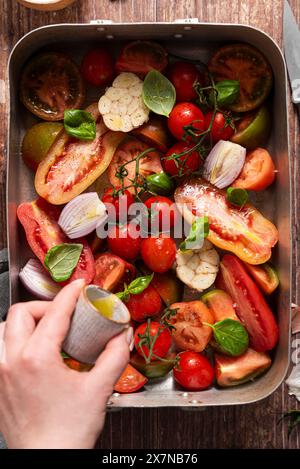 Hand pouring olive oil on tomato bake Stock Photo