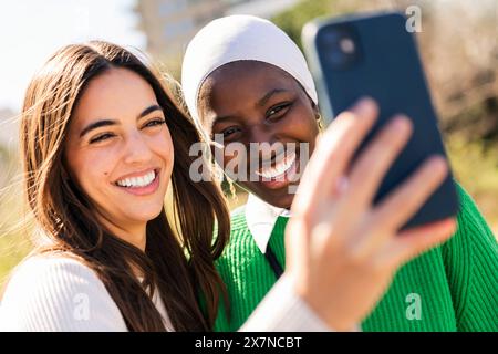 two young female friends smiling happy and having fun taking selfie photo with mobile phone, concept of diversity and modern lifestyle Stock Photo