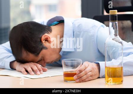 Cropped shot of a stressed businessman holding a glass of whiskey he sleeping and Data Charts,business document at office desk. alcohol addiction and Stock Photo