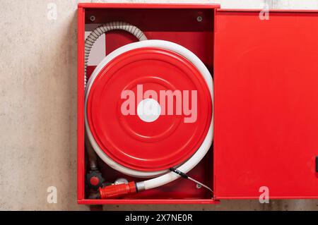Red fire hose reel, mounted on a concrete wall background. Stock Photo