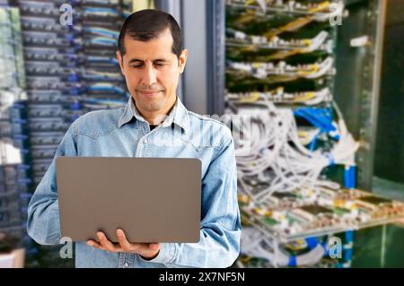 Waist up portrait of man as network engineer in server room using laptop Stock Photo