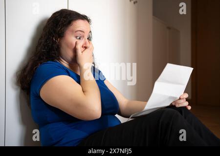 Sad woman complaining reading a letter in the night sitting on a floor at home Stock Photo