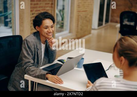 Two stylish smiling female sales managers talking during work while sitting in cozy office Stock Photo