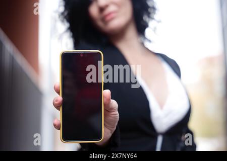 Happy woman smiling pointing to empty smartphone screen outdoors Stock Photo