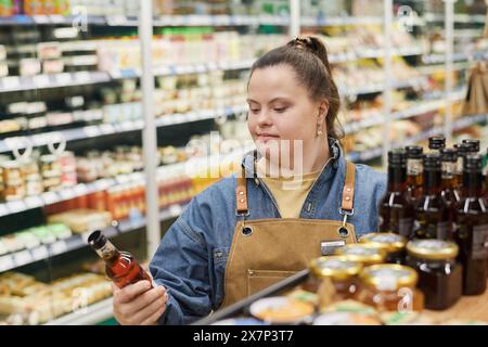 Waist up portrait of smiling young woman with Down syndrome working in supermarket and inspecting stock on shelves copy space Stock Photo