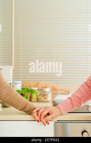 Close up picture of a senior couple holding hands in the kitchen, showcasing a tender moment of connection and affection. Stock Photo