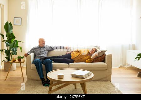 Senior married couple relaxing on a sofa in their living room. Senior couple lying down on a sofa enjoying a peaceful and comfortable moment at home. Stock Photo