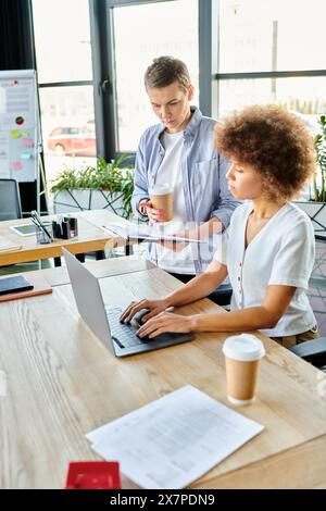 Two diverse women collaborating on a laptop at a table in a modern workspace. Stock Photo