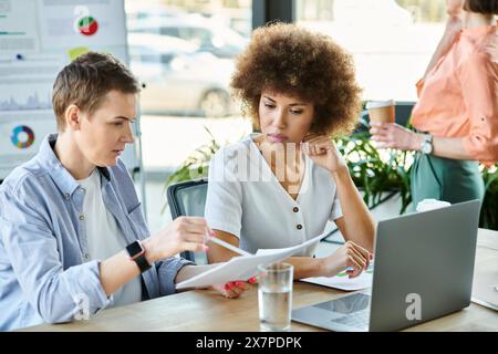 Diverse businesswomen sit together at a table, focusing on paperwork and discussing business matters. Stock Photo