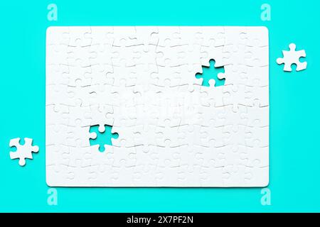 Blank white rectangular puzzle with two final pieces set aside on a serene blue background. Challenge and creativity related concept. Stock Photo