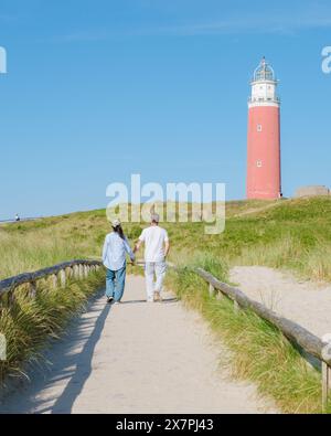 Two individuals strolling along a path near a charming lighthouse in Texel, Netherlands, enjoying the serene coastal scenery. a couple of men and women at The iconic red lighthouse of Texel Netherlands Stock Photo
