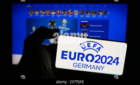 Person holding mobile phone with logo of European football championship UEFA Euro 2024 in front of web page. Focus on phone display. Stock Photo