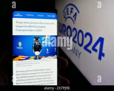 Person holding cellphone with webpage of European football championship UEFA Euro 2024 in front of logo. Focus on center of phone display. Stock Photo