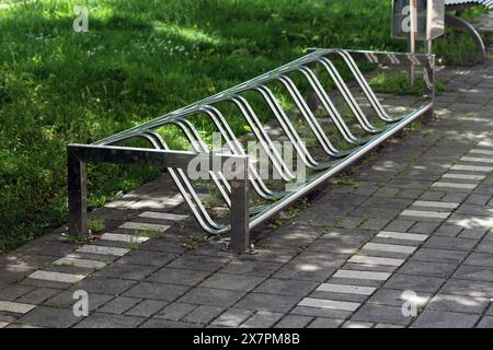 Modern new floor mounted public bike stand or bike rack on top of stone tiles sidewalk next to uncut grass at local public park on warm sunny spring Stock Photo