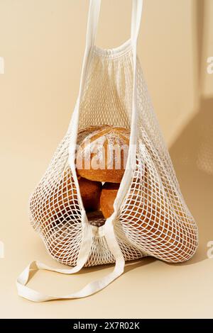 Various freshly baked sourdough breads nestled in an eco-friendly mesh bag, highlighted by a warm beige background. Stock Photo