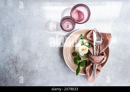 An exquisite table setting showcasing beige plates, white roses, and rustic utensils on a textured background Stock Photo