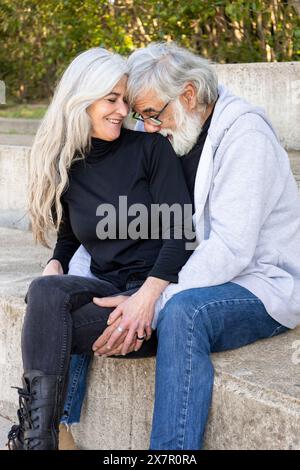 An affectionate elderly couple sitting closely together on outdoor steps, expressing love and companionship with gentle smiles and intertwined hands Stock Photo