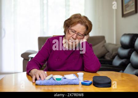 Senior woman appears distressed and exhausted as she leans on her hand at home, with diabetes monitoring tools visibly placed on the table next to her Stock Photo