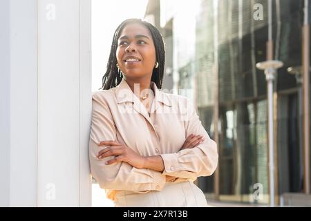 Confident young woman with braided hair smiles in the Barcelona sun, standing casually with arms crossed Stock Photo
