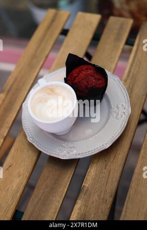 A fresh red velvet muffin paired with a hot cappuccino on a vintage plate, set on a wooden table for a relaxing coffee break Stock Photo