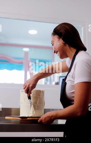 A woman in a home kitchen smiles while frosting a cake with precision and care Stock Photo