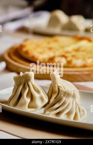 A delicious selection of Georgian cuisine, featuring khinkali dumplings on a ceramic plate and khachapuri cheese bread on a wooden serving board in th Stock Photo