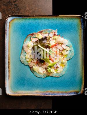 An appetizing seafood salad featuring mixed seafood, fresh lettuce, and vibrant vegetables, elegantly served on a textured blue ceramic plate against Stock Photo