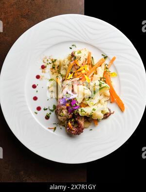 A meticulously prepared gourmet dish features seafood, julienne carrots, and colorful edible flowers, artistically plated on a white dish against a da Stock Photo