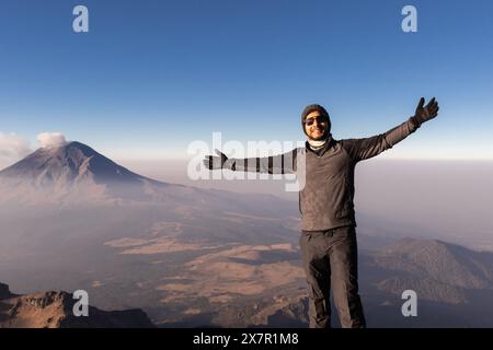 Joyful hiker with open arms stands atop Iztaccihuatl volcano with misty landscape in background Stock Photo