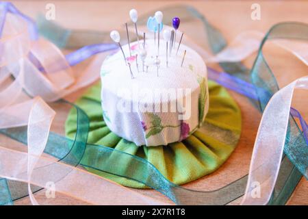 A vibrant pin cushion adorned with needles and surrounded by a selection of multicolored ribbons resting on a wooden surface, highlighting essential t Stock Photo