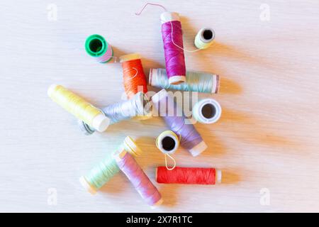 A variety of colorful thread spools scattered atop a light wooden surface, symbolizing sewing and design Stock Photo