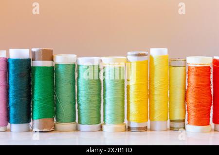 A vibrant array of colored sewing thread spools lined up on a table, showcasing materials for sewing and design Stock Photo