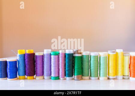 A colorful arrangement of sewing thread spools in various colors lined up against a soft, neutral background, symbolizing organization and preparation Stock Photo