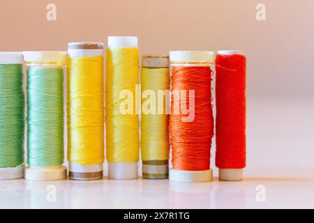 An array of sewing thread spools in shades of green, yellow, and red, neatly aligned against a pale background Stock Photo