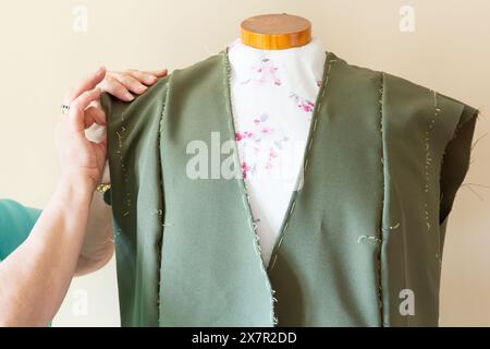 Close-up of a tailor fitting a green garment on a mannequin, with floral lining and hand stitches visible Stock Photo