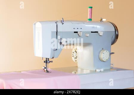 An industrial sewing machine with a spool of green thread set up on a textile-covered table, ready for crafting in a designer workshop Stock Photo