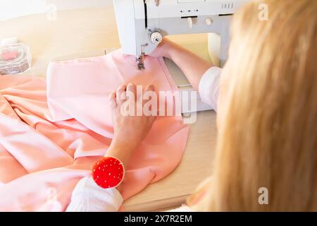 Close-up of a tailor's hands working with pink fabric on a sewing machine in a design workshop Stock Photo