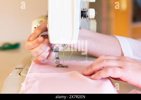 A detailed close-up showing a person's hands working on a pink fabric with a sewing machine during a sewing and design workshop Stock Photo