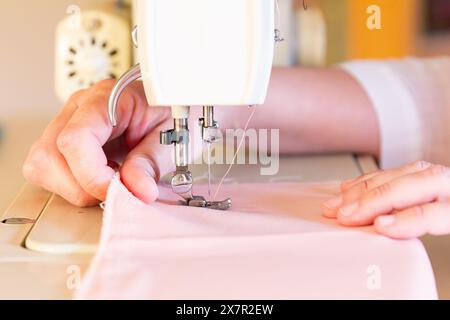 A detailed view of a sewing machine in action, with hands guiding pink fabric under the needle, emphasizing the creative process in a design workshop Stock Photo