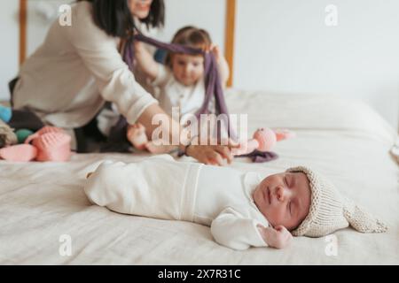 A heartwarming scene captures a mother playing with her toddler while a newborn baby sleeps peacefully on the bed, surrounded by soft toys and wearing Stock Photo