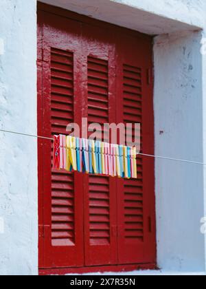 Colorful clothespins line up on a string against a rustic red door with shutters. Stock Photo