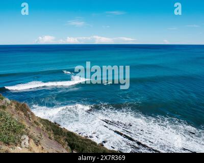 Tranquil coastal seascape with gentle waves breaking on rocky shoreline under a clear blue sky. Stock Photo