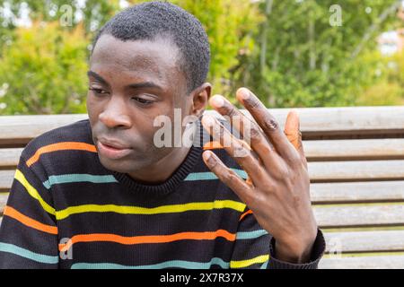 A middle-aged black man showing signs of distress, possibly experiencing hypoglycemia, while sitting on a park bench Stock Photo