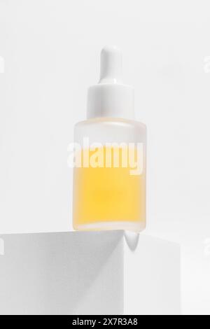 Minimalist image of a cosmetics serum bottle with a bright yellow serum showcased on a geometric pedestal. Stock Photo